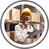 A foreman holds a clip board and looks around a storage shed. 